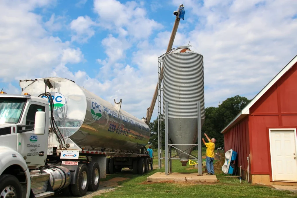 pexels-photo-5368132 A truck unloading grain at a silo beside a red barn on a farm.